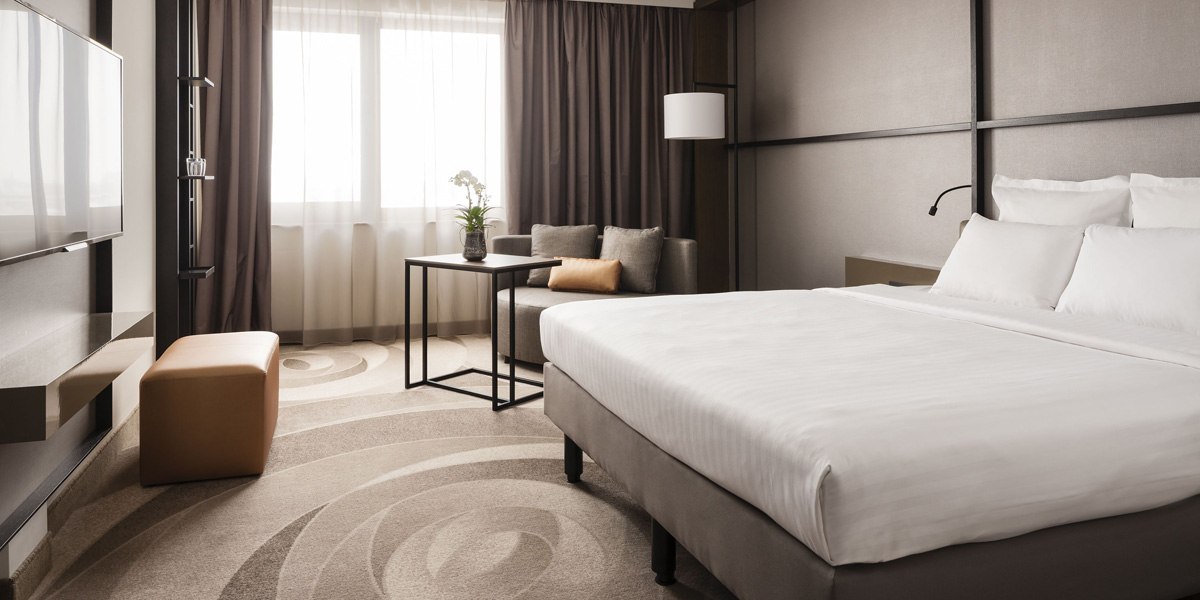 Modern hotel room with large bed, sofa, table and TV. Light curtains and subtle colors create an elegant atmosphere., © Stuttgart Marriott Hotel Sindelfingen Modern hotel room with large bed, sofa, table and TV. Light curtains and subtle colors create an elegant atmosphere., © Stuttgart Marriott Hotel Sindelfingen