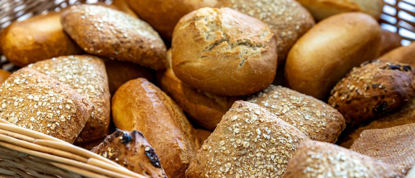 Ein Korb voller verschiedener Brötchen, darunter Vollkorn- und Weizenbrötchen, teilweise mit Körnern bestreut., © PLAZA INN Rieker Stuttgart Hauptbahnhof Ein Korb voller verschiedener Brötchen, darunter Vollkorn- und Weizenbrötchen, teilweise mit Körnern bestreut., © PLAZA INN Rieker Stuttgart Hauptbahnhof