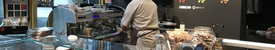 A barista in a caf&eacute; prepares coffee. In front of him are pastries, a coffee machine and packets of tea., &copy; Old Bridge, Stuttgart