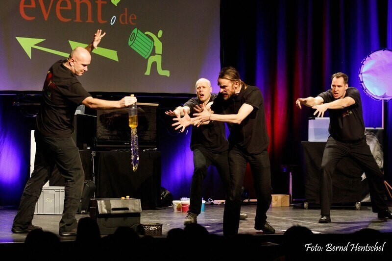 Four men on a stage perform a dynamic physics show. One holds a bottle while the others gesticulate. Colorful lights in the background., &copy; Theaterhaus Stuttgart e.V.