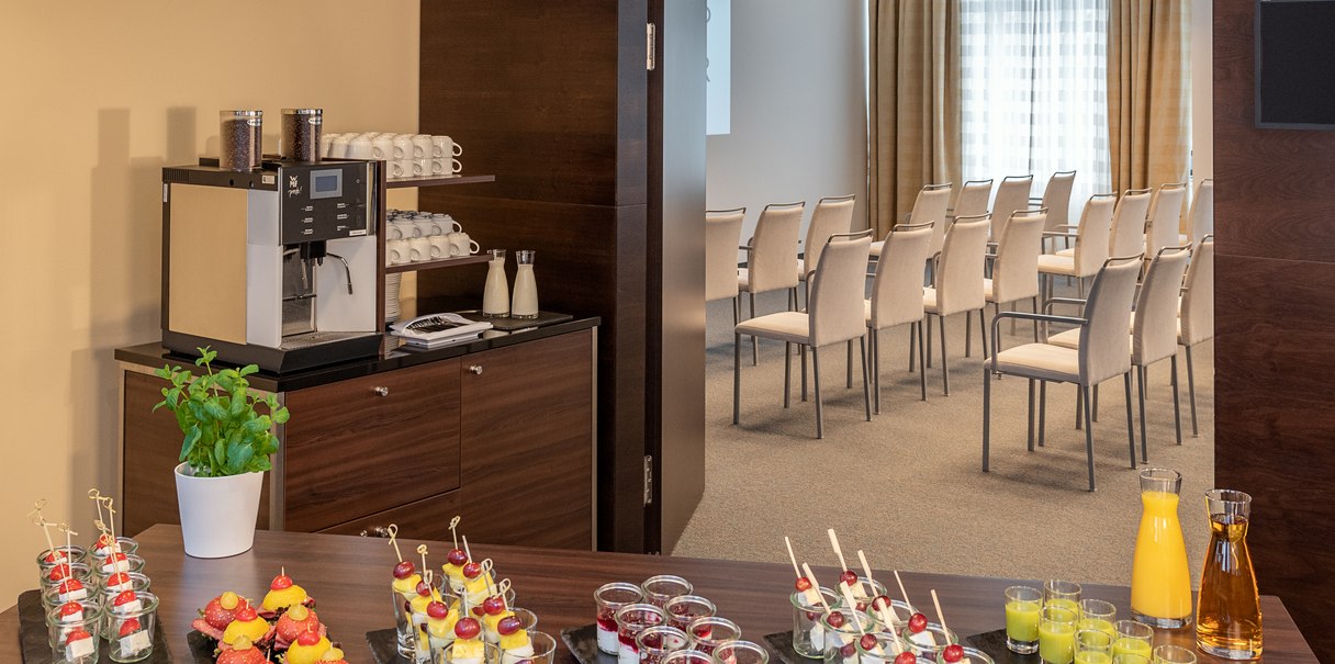 Ein Konferenzraum mit Stuhlreihen und einem Tisch mit Snacks, Getr&auml;nken und einer Kaffeemaschine im Vordergrund., &copy; NH Hotel Stuttgart Airport