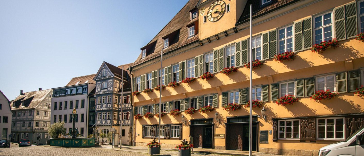 Historic buildings on Nürtingen's market square with half-timbered houses and floral decorations. The sun shines on the facades, which are decorated with red flowers., © Stuttgart-Marketing GmbH, Sarah Schmid Historic buildings on Nürtingen's market square with half-timbered houses and floral decorations. The sun shines on the facades, which are decorated with red flowers., © Stuttgart-Marketing GmbH, Sarah Schmid