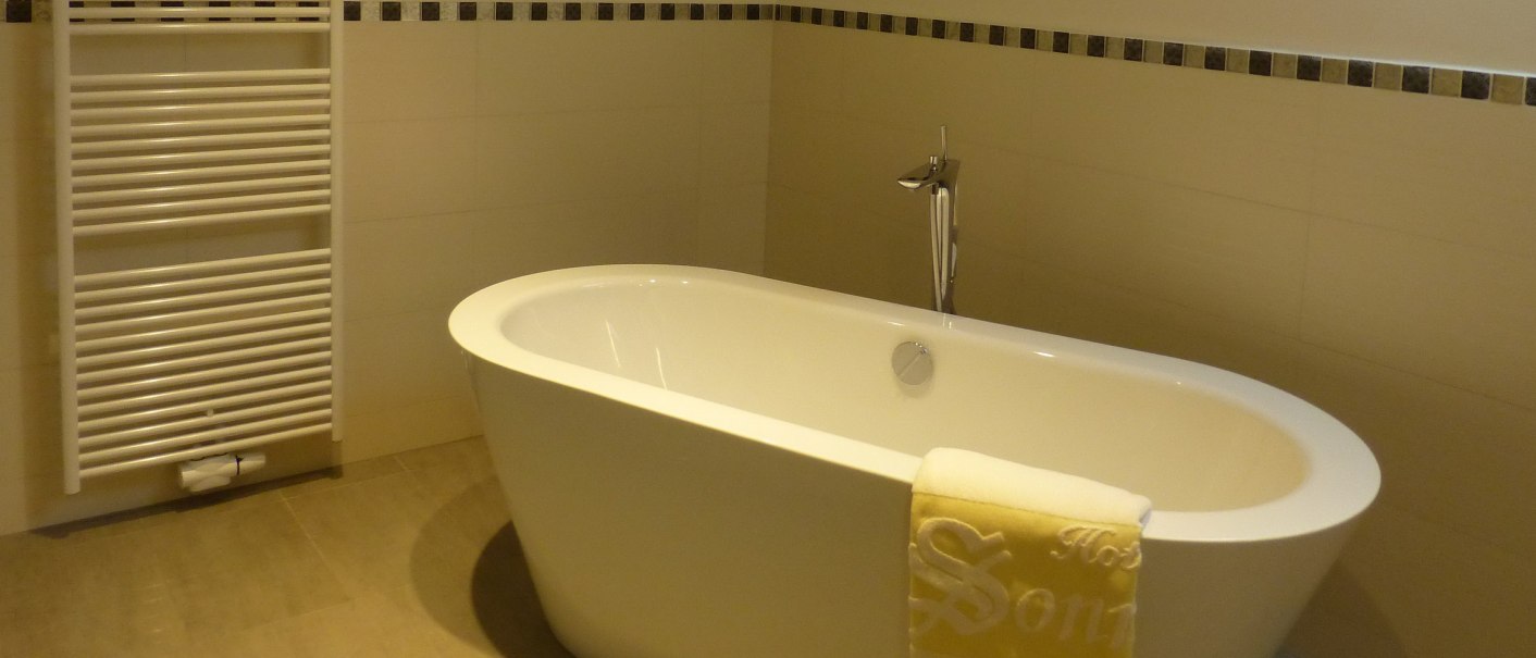 Freestanding bathtub in a modern bathroom with towel and radiator on the wall., © Hotel & Restaurant Sonne