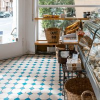 A delicatessen with cheese display, pastries and bottles of wine. Light-colored tiles and a window with a view of the street., &copy; SMG, Sarah Schmid