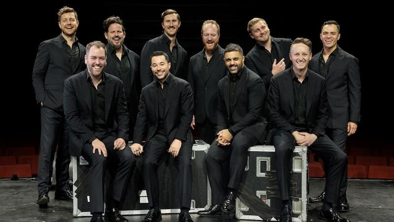 Zehn Männer in schwarzen Anzügen posieren lächelnd auf einer Bühne. Einige sitzen auf Kisten, andere stehen dahinter. Sie wirken fröhlich und entspannt., © Music Circus Concertbüro GmbH &CoKG Zehn Männer in schwarzen Anzügen posieren lächelnd auf einer Bühne. Einige sitzen auf Kisten, andere stehen dahinter. Sie wirken fröhlich und entspannt., © Music Circus Concertbüro GmbH &CoKG