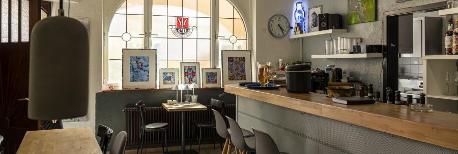 Gem&uuml;tliches Caf&eacute; mit Holztresen, Kunstwerken an den W&auml;nden und einem gro&szlig;en Fenster. Eine Uhr und Dekorationen schm&uuml;cken den Raum., &copy; SMG, Sarah Schmid