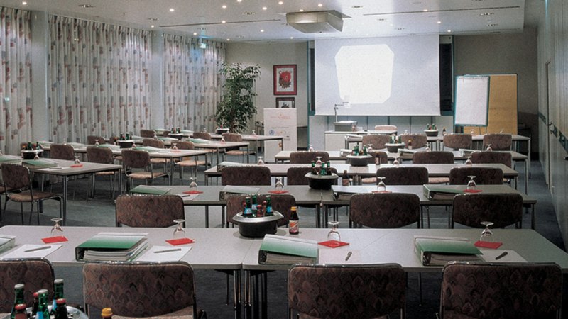 Ein leerer Konferenzraum mit Tischen, Stühlen, einem Projektor und einem Flipchart. Auf den Tischen liegen Ordner und Wasserflaschen., © © H-Hotels.com Ein leerer Konferenzraum mit Tischen, Stühlen, einem Projektor und einem Flipchart. Auf den Tischen liegen Ordner und Wasserflaschen., © © H-Hotels.com