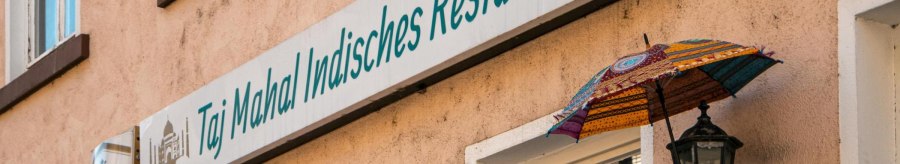 Fassade eines indischen Restaurants in Stuttgart mit bunten Schirmen und einem Schild mit der Aufschrift 'Taj Mahal Indisches Restaurant'., &copy; SMG, Sarah Schmid