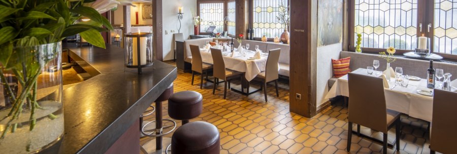 A cozy restaurant with a wooden beamed ceiling, set tables and large windows. Flowers and candles create an inviting atmosphere., © Hotel Gloria GmbH