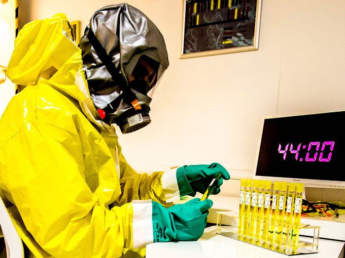 Person in yellow protective suit and breathing mask works with samples. A timer indicates 44:00. Laboratory environment with test tubes., © ExitGames Stuttgart Person in yellow protective suit and breathing mask works with samples. A timer indicates 44:00. Laboratory environment with test tubes., © ExitGames Stuttgart