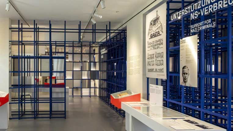 Ein Ausstellungsraum mit blauen Gitterstrukturen, historischen Plakaten und Informationsmaterialien an den Wänden., © Haus der Geschichte Baden-Württemberg Ein Ausstellungsraum mit blauen Gitterstrukturen, historischen Plakaten und Informationsmaterialien an den Wänden., © Haus der Geschichte Baden-Württemberg