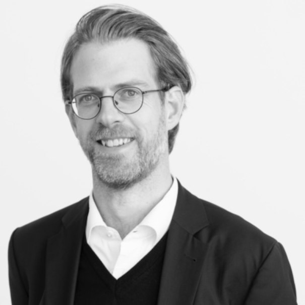 Ein Mann mit Brille und Bart lächelt in die Kamera. Er trägt einen Anzug und ein Hemd. Das Bild ist in Schwarz-Weiß gehalten., © Renitenztheater Stuttgart e.V. Ein Mann mit Brille und Bart lächelt in die Kamera. Er trägt einen Anzug und ein Hemd. Das Bild ist in Schwarz-Weiß gehalten., © Renitenztheater Stuttgart e.V.