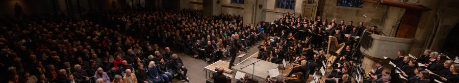 Ein Orchester und Chor führen in einer Kirche vor einem großen Publikum auf. Die Kirche hat hohe Fenster und eine Orgel., © www.hassfoto.de