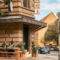 A street corner with a butcher's shop. Two people are sitting at a table in front of the store. A car drives past and there is a traffic light., &copy; SMG, Sarah Schmid