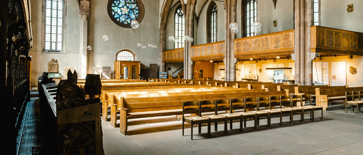 Innenansicht der Leonardskirche mit Holzb&auml;nken, Buntglasfenstern und h&ouml;lzernen Deckenbalken. Die Architektur ist gotisch gepr&auml;gt., &copy; SMG Stuttgart Marketing GmbH - Sarah Schmid
