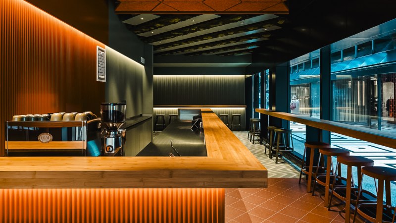 Modern bar with wooden counter, stools and stylish lighting in the Shobu Calwer Passage. Dark walls and geometric ceiling patterns., © Blackbook Studios