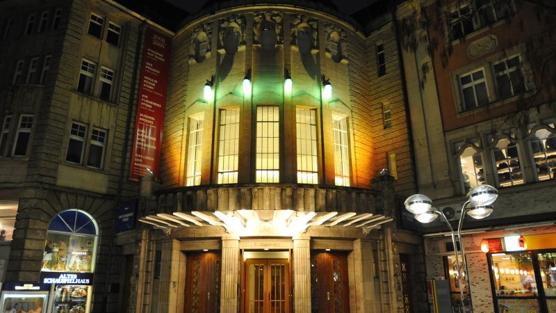 Das Alte Schauspielhaus bei Nacht, beleuchtet mit bunten Lichtern. Der Eingang ist von historischen Gebäuden umgeben., © Schauspielbühnen Stuttgart Das Alte Schauspielhaus bei Nacht, beleuchtet mit bunten Lichtern. Der Eingang ist von historischen Gebäuden umgeben., © Schauspielbühnen Stuttgart