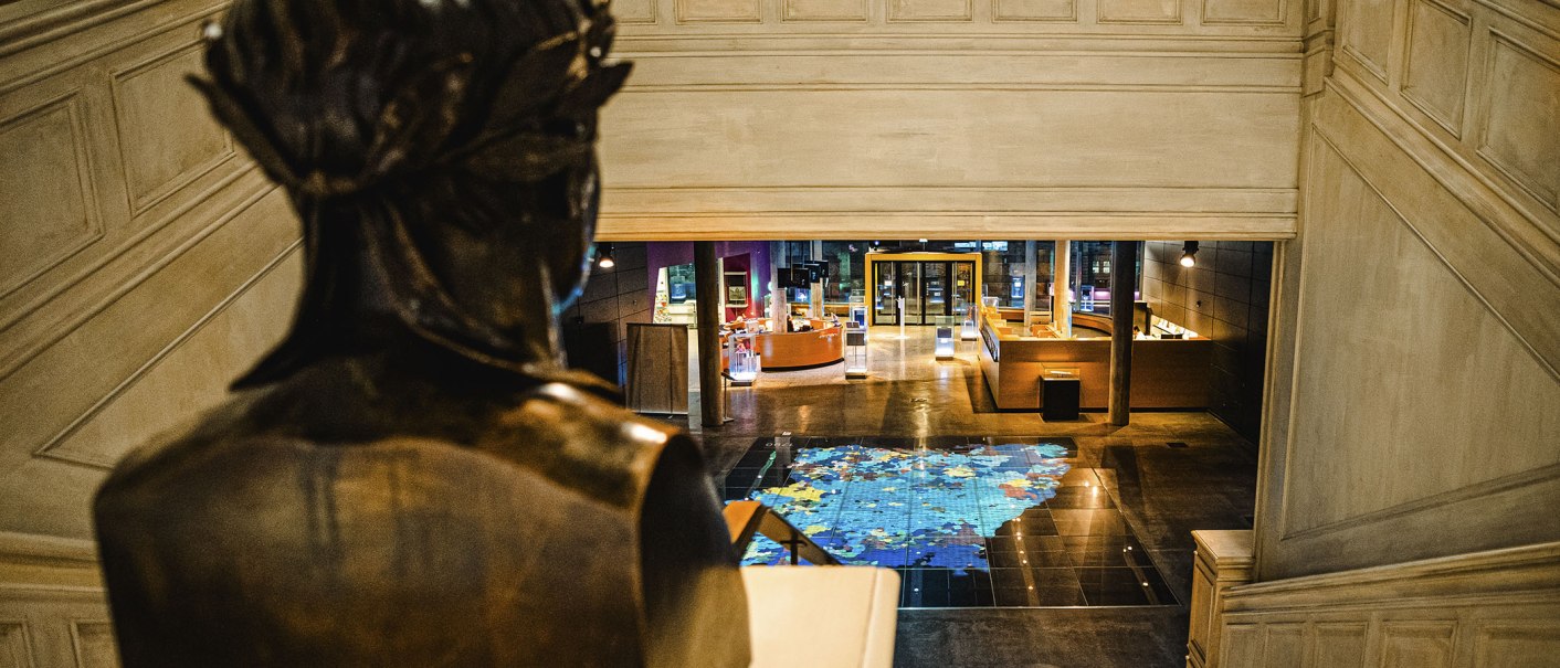 Eine Statue blickt auf eine Ausstellungshalle mit einer großen Bodenkarte und modernen Displays im Haus der Geschichte., © Stuttgart Marketing GmbH, Sarah Schmid Eine Statue blickt auf eine Ausstellungshalle mit einer großen Bodenkarte und modernen Displays im Haus der Geschichte., © Stuttgart Marketing GmbH, Sarah Schmid