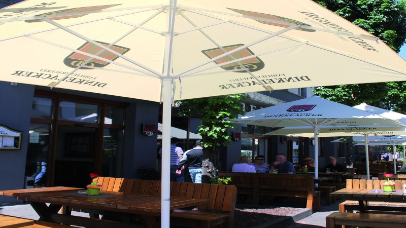 Außenbereich der Brauereigaststätte Dinkelacker mit Holzbänken und Sonnenschirmen. Gäste sitzen im Schatten und genießen das Wetter., © Stuttgart-Marketing GmbH