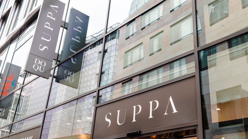 Glass fa&ccedil;ade of a modern building with several SUPPA signs. The reflection shows the surrounding architecture., &copy; Sarah Schmid