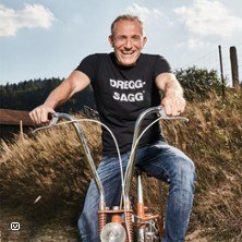 Mann auf Fahrrad mit "Dregg-Sagg" T-Shirt, l&auml;chelnd vor l&auml;ndlicher Kulisse., &copy; links im Bild