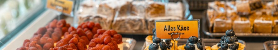Kuchen in einer Vitrine, dekoriert mit Himbeeren und Blaubeeren. Ein Schild mit der Aufschrift 'Alles Käse' ist sichtbar., © Stuttgart-Marketing GmbH, Sarah Schmid