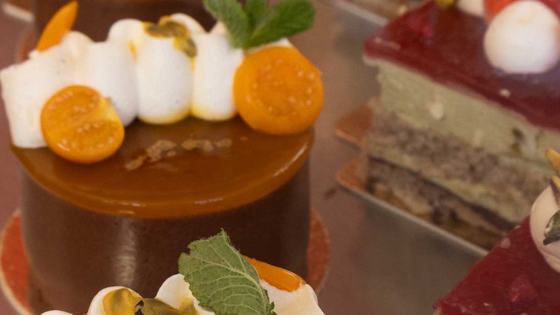 Close-up of artfully decorated cakes in a display case. Various toppings such as fruit and cream can be seen., © SMG
