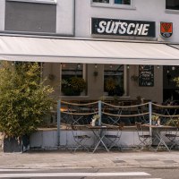 Café 'Sutsche' with outdoor area, tables and chairs on the sidewalk, surrounded by plants., © SMG Stuttgart Marketing GmbH - Sarah Schmid Café 'Sutsche' with outdoor area, tables and chairs on the sidewalk, surrounded by plants., © SMG Stuttgart Marketing GmbH - Sarah Schmid