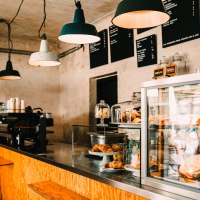 Ein gem&uuml;tliches Caf&eacute; mit Holztresen, Kaffeemaschine und Geb&auml;ck in einer Glasvitrine. H&auml;ngelampen beleuchten den Raum., &copy; Melanie Mearz Fotografie