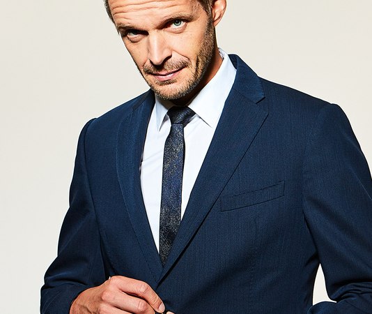 Ein Mann in einem dunkelblauen Anzug kn&ouml;pft sein Jackett zu und schaut selbstbewusst in die Kamera., &copy; Theaterhaus Stuttgart e.V.