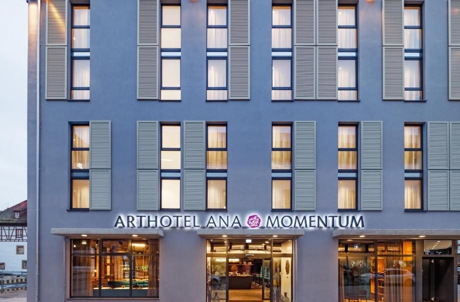 Façade of the Arthotel Ana Momentum with large windows and illuminated entrance. Modern architecture with blue shutters., © Arthotel ANA Momentum Façade of the Arthotel Ana Momentum with large windows and illuminated entrance. Modern architecture with blue shutters., © Arthotel ANA Momentum
