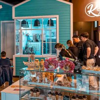 Gem&uuml;tliches Caf&eacute; mit G&auml;sten an Tischen, Personal hinter der Theke. Dekorative Beleuchtung und bunte Einrichtung schaffen eine einladende Atmosph&auml;re., &copy; Kesselgl&uuml;ck