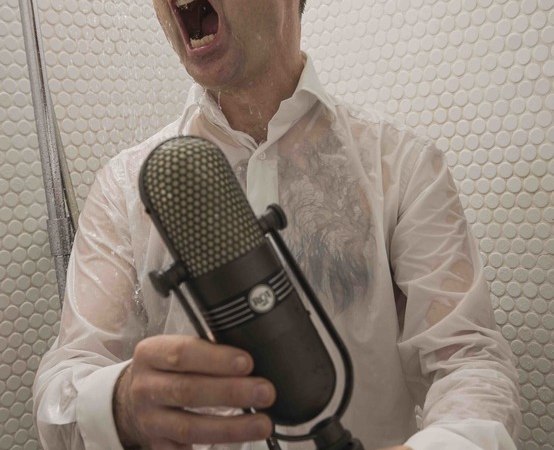 Ein Mann in einem nassen Hemd singt leidenschaftlich in ein Mikrofon unter der Dusche. Die Szene wirkt humorvoll und energiegeladen., &copy; Rosenau Kultur e.V.