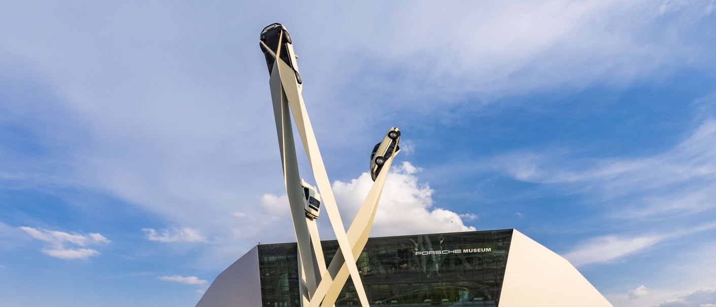 The Porsche Museum with its modern architecture and a sculpture of three cars on high pillars against a blue sky., © Stuttgart-Marketing GmbH, Werner Dieterich