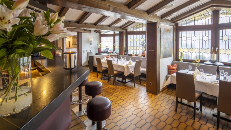 Ein gemütliches Restaurant mit Holzbalkendecke, gedeckten Tischen und großen Fenstern. Blumen und Kerzen sorgen für eine einladende Atmosphäre., © Hotel Gloria GmbH Ein gemütliches Restaurant mit Holzbalkendecke, gedeckten Tischen und großen Fenstern. Blumen und Kerzen sorgen für eine einladende Atmosphäre., © Hotel Gloria GmbH