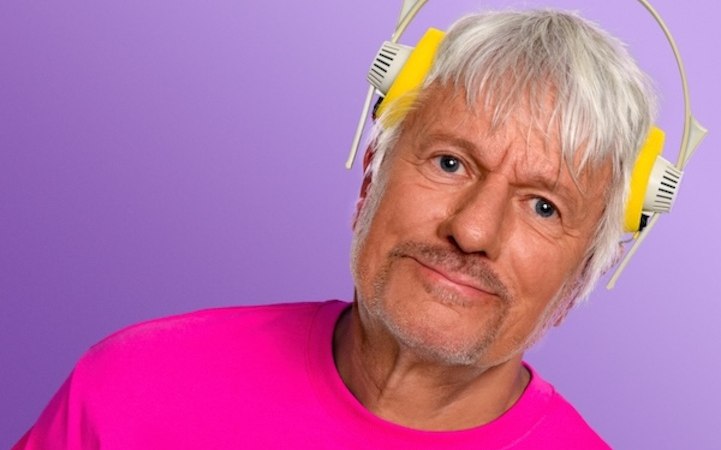 Ein Mann mit grauen Haaren tr&auml;gt gelbe Kopfh&ouml;rer und ein pinkes T-Shirt vor einem lila Hintergrund., &copy; Renitenztheater Stuttgart e.V.