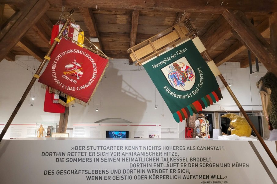 Traditionelle Fahnen und Masken im Stadtmuseum Bad Cannstatt. Ein Zitat von Heinrich Ebner ist an der Wand zu sehen., © StadtPalais