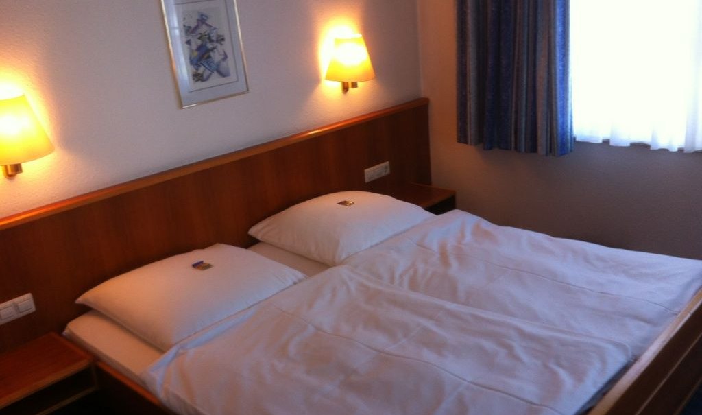 Ein gemütliches Doppelzimmer mit einem großen Bett, zwei Wandlampen und einem Bild an der Wand. Ein Fenster mit Vorhängen ist zu sehen., © Hotel Sonne garni Ein gemütliches Doppelzimmer mit einem großen Bett, zwei Wandlampen und einem Bild an der Wand. Ein Fenster mit Vorhängen ist zu sehen., © Hotel Sonne garni