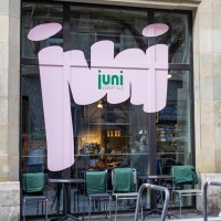 A caf&eacute; with large windows and the words 'juni essentials'. In front of it are bicycles and tables with chairs., &copy; SMG, Sarah Schmid