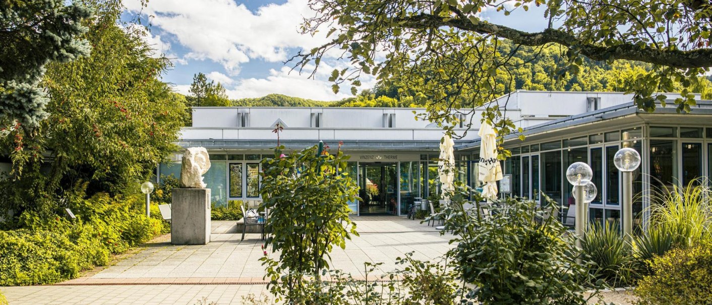 The entrance to the Vinzenz Therme in Bad Ditzenbach, surrounded by lush greenery and a sunny sky., © SMG Stuttgart Marketing GmbH - Sarah Schmid The entrance to the Vinzenz Therme in Bad Ditzenbach, surrounded by lush greenery and a sunny sky., © SMG Stuttgart Marketing GmbH - Sarah Schmid