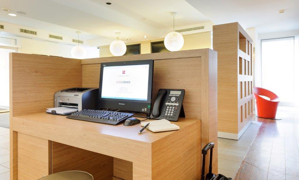 Moderner Arbeitsbereich mit Computer, Drucker und Telefon in einem hellen Raum. Ein roter Stuhl steht im Hintergrund., © Ibis Stuttgart Airport Messe