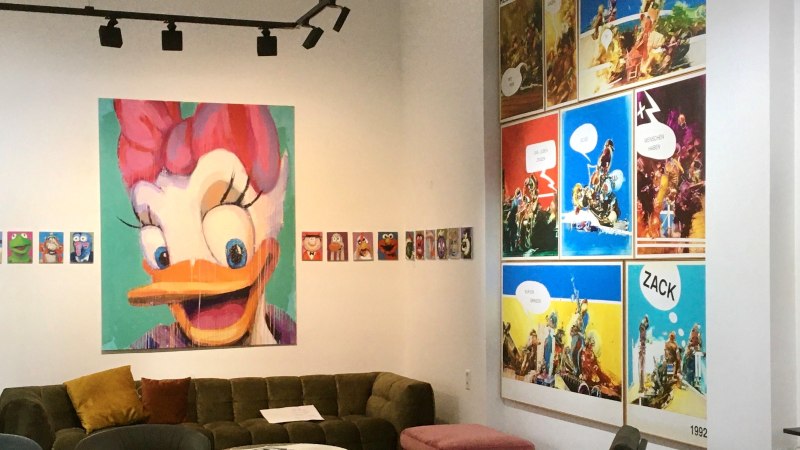 Eine Galerie zeigt bunte Pop-Art-Gemälde von Comicfiguren und moderne Kunstwerke. Ein großes Bild einer Ente dominiert die Wand. Ein Sofa steht im Raum., © GALERIE Z Eine Galerie zeigt bunte Pop-Art-Gemälde von Comicfiguren und moderne Kunstwerke. Ein großes Bild einer Ente dominiert die Wand. Ein Sofa steht im Raum., © GALERIE Z