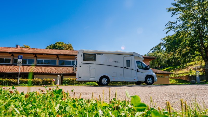 Wohnmobil auf einem Parkplatz vor einem Gebäude mit rotem Dach, umgeben von Bäumen und grünem Gras., © Stuttgart-Marketing GmbH, Thomas Niedermüller