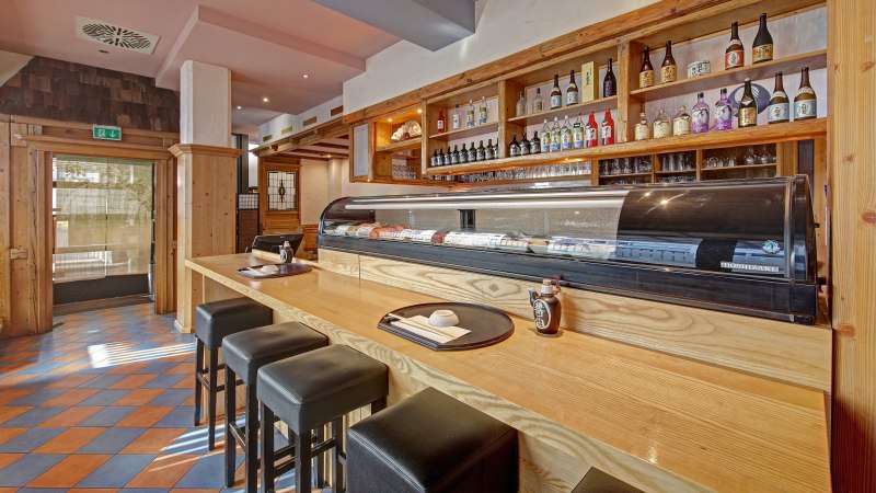 A Japanese restaurant with a sushi counter, bar stools and shelves full of sake bottles. Wooden elements dominate the interior., © Martin Frey