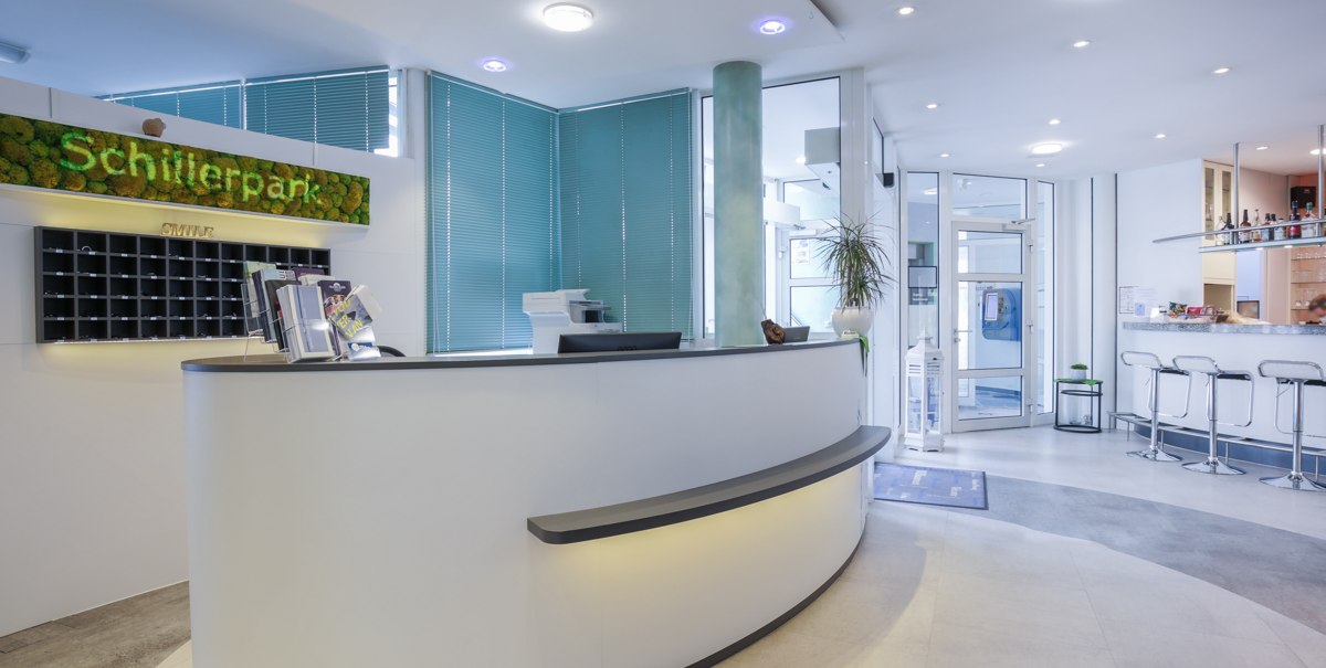 Moderne Rezeption mit geschwungenem Tresen, gr&uuml;ner Dekoration und Barbereich im Hintergrund. Helle, einladende Atmosph&auml;re., &copy; TOMAS