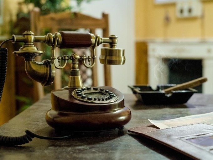 Ein antikes Telefon steht auf einem Tisch. Daneben ein rauchender Aschenbecher und ein offener Ordner. Im Hintergrund ein Stuhl und ein Kamin., © ExitGames Stuttgart Ein antikes Telefon steht auf einem Tisch. Daneben ein rauchender Aschenbecher und ein offener Ordner. Im Hintergrund ein Stuhl und ein Kamin., © ExitGames Stuttgart