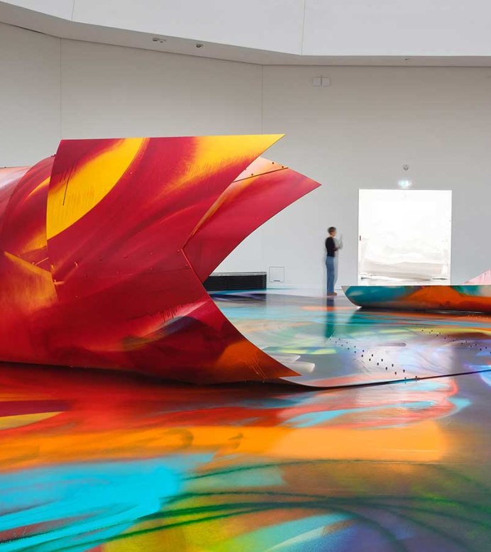 Bunte, großflächige Installation von Katharina Grosse in einer Galerie. Zwei Personen betrachten die farbenfrohen Strukturen und den bemalten Boden., © VG Bild-Kunst, Bonn 2025