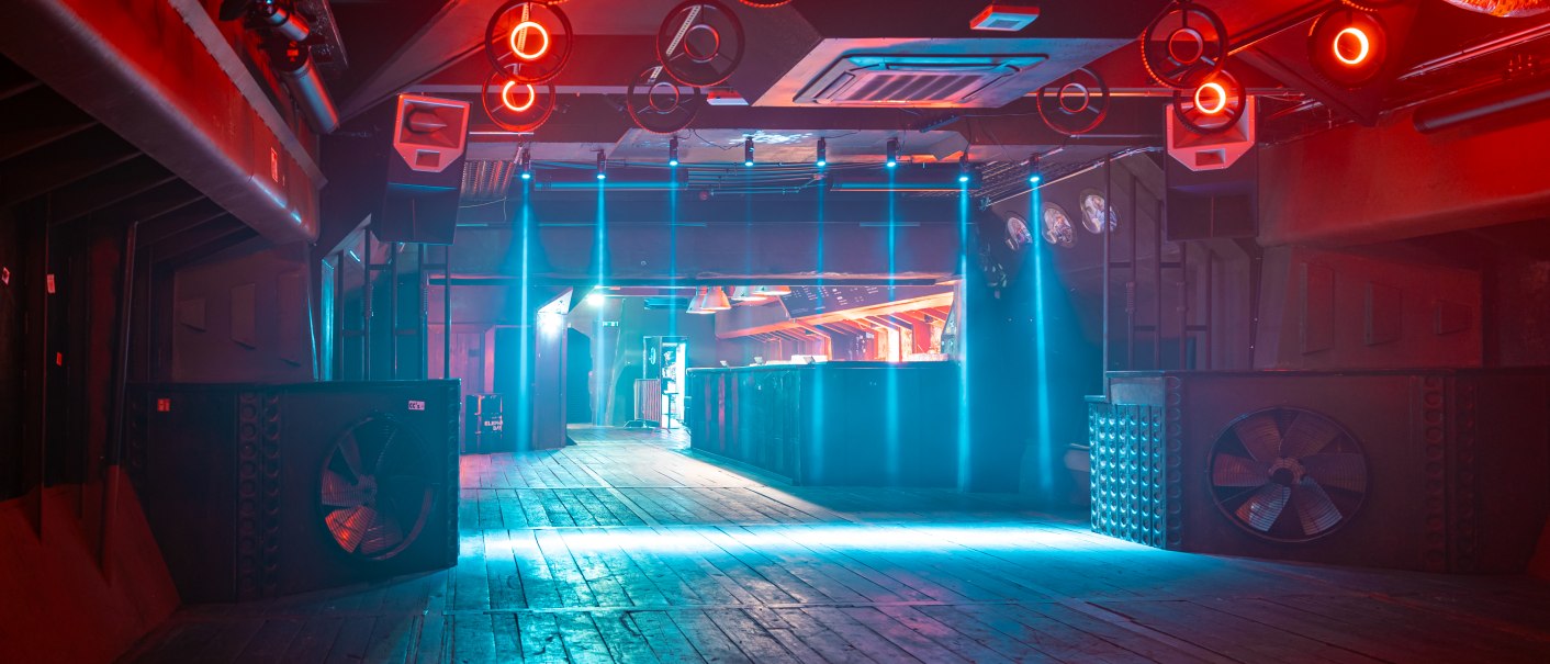 Leerer Nachtclub mit Holzboden, roter und blauer Beleuchtung. An der Decke hängen runde Lichter, im Hintergrund ist eine Bar zu sehen., © SMG Stuttgart Marketing GmbH, Sarah Schmid