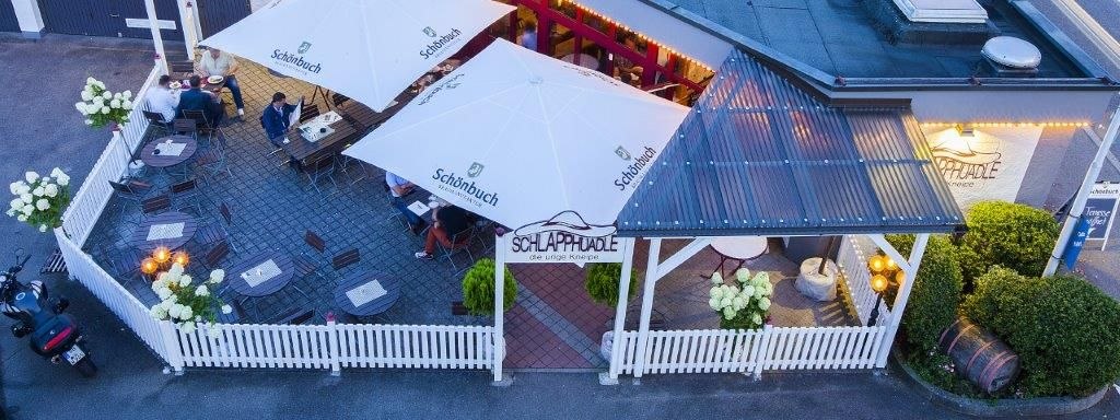 A patio with white umbrellas and wooden furniture, surrounded by a white fence. People are sitting at tables decorated with flowers., &copy; Hotel Waldhorn