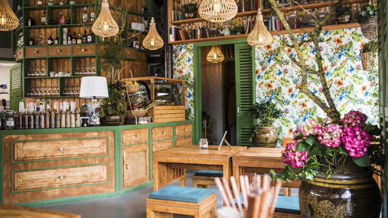 Gemütlicher Gastraum mit Holzmöbeln, bunten Blumen, Regalen voller Flaschen und Büchern. Helle Lampen und florale Tapete schaffen eine einladende Atmosphäre., © Vietal Kitchen Gemütlicher Gastraum mit Holzmöbeln, bunten Blumen, Regalen voller Flaschen und Büchern. Helle Lampen und florale Tapete schaffen eine einladende Atmosphäre., © Vietal Kitchen